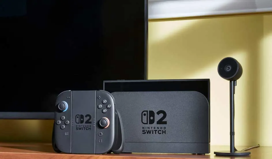 Console Nintendo Switch grise, dock, manette et caméra noire sur une table en bois. Écran de téléviseur en arrière-plan.