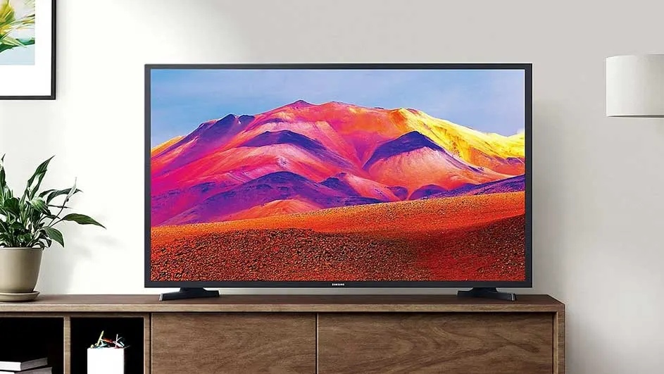 Een zwarte tv staat op een houten kast. Het scherm toont een kleurrijk berglandschap onder een blauwe lucht.