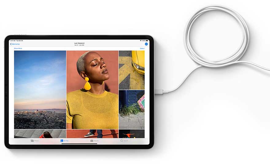 Tablette noire affichant une galerie de photos avec un câble blanc connecté, sur fond blanc.