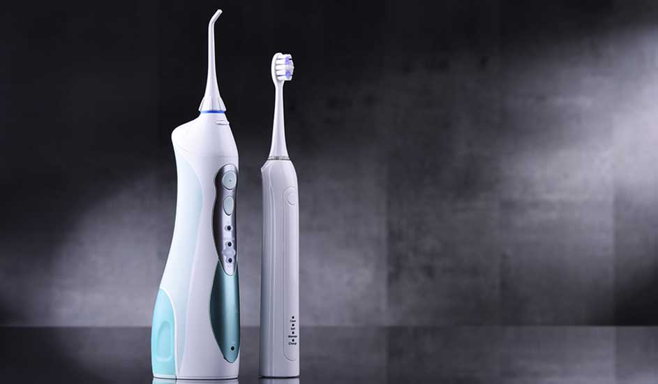 Un hydropulseur blanc et une brosse à dents électrique se tiennent sur une surface grise devant un fond sombre.