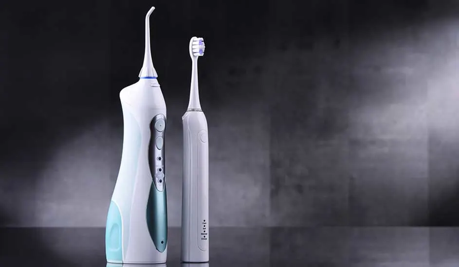Un hydropulseur blanc et une brosse à dents électrique se tiennent sur une surface grise devant un fond sombre.