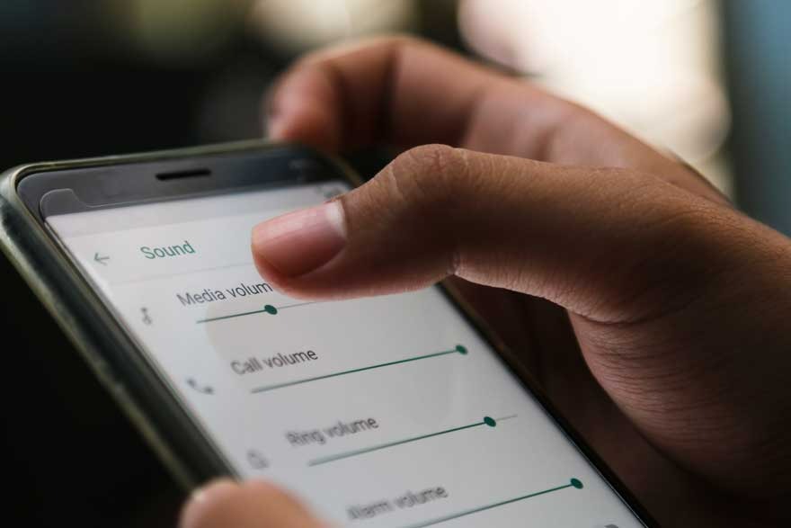 Gros plan d'un téléphone affichant les paramètres audio, un doigt ajustant le volume des médias sur un écran blanc.