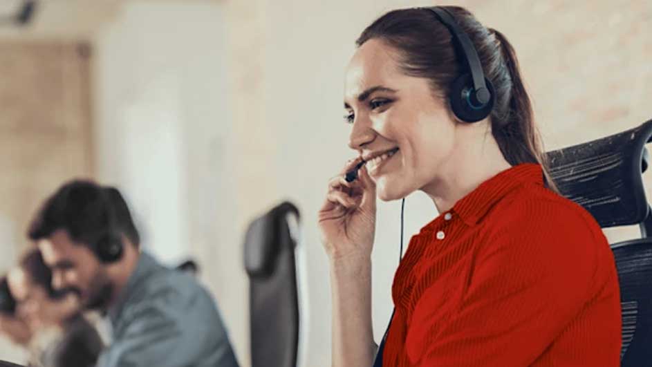 Een kantoorafbeelding met een vrouw in een rode blouse en een headset. Andere mensen en bureaustoelen zijn op de achtergrond te zien.
