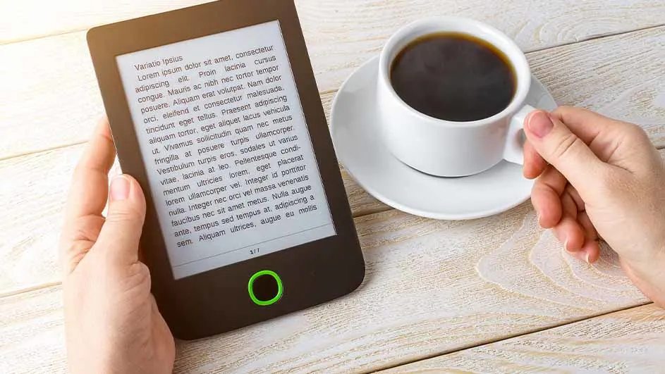 E-reader met tekst naast een witte koffiekop op een schotel, op een houten tafel.