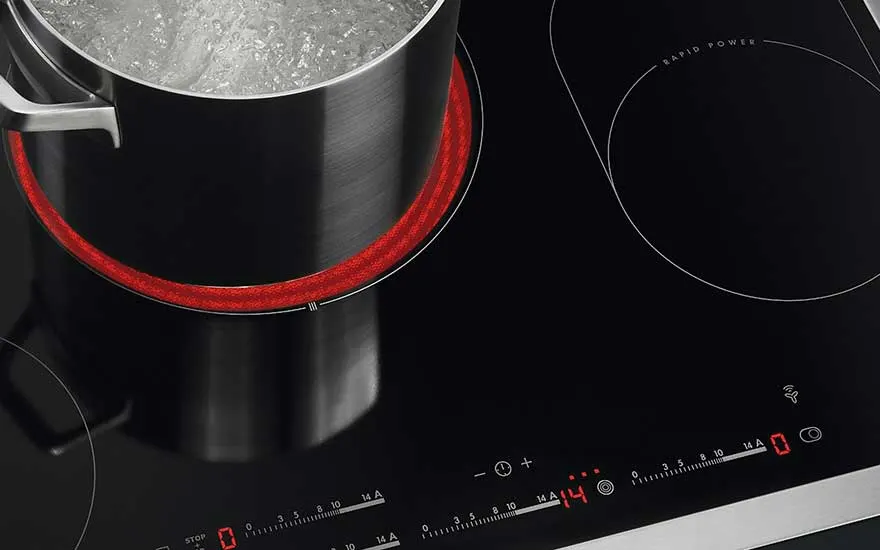 Een zwarte inductiekookplaat met een kookpot erop, de kookzone is roodgloeiend. Het bedieningspaneel toont warmte-instellingen.