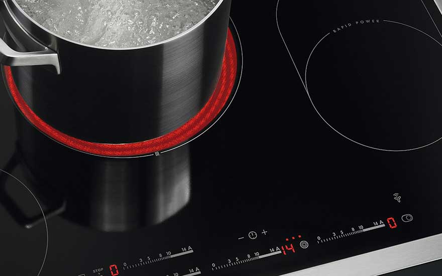 Een zwarte inductiekookplaat met een kookpot erop, de kookzone is roodgloeiend. Het bedieningspaneel toont warmte-instellingen.