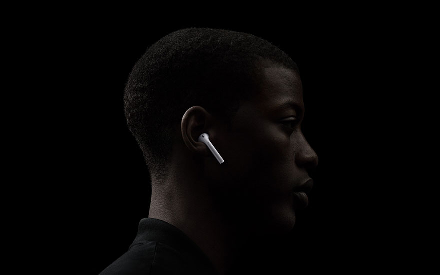 Profil sur fond noir : un écouteur blanc dans l'oreille, éclairé, avec un col de chemise sombre visible.