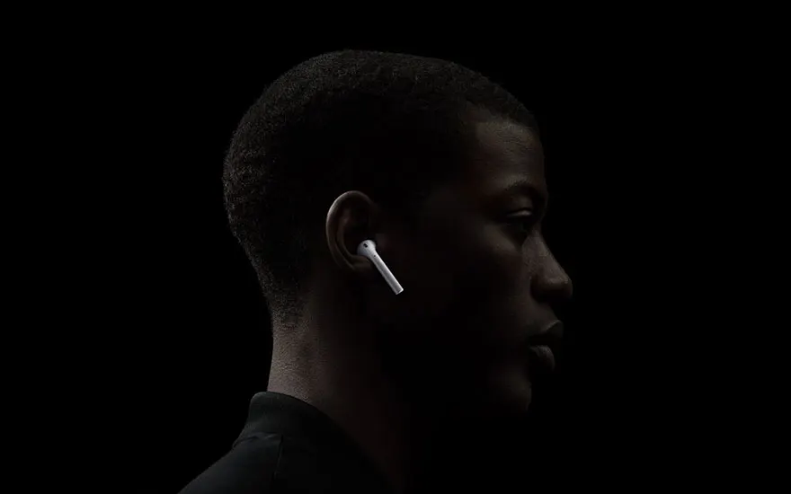 Profil sur fond noir : un écouteur blanc dans l'oreille, éclairé, avec un col de chemise sombre visible.