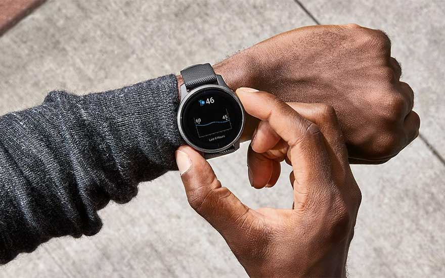 Gros plan sur une montre noire affichant des données sur un poignet, sur fond de béton clair.
