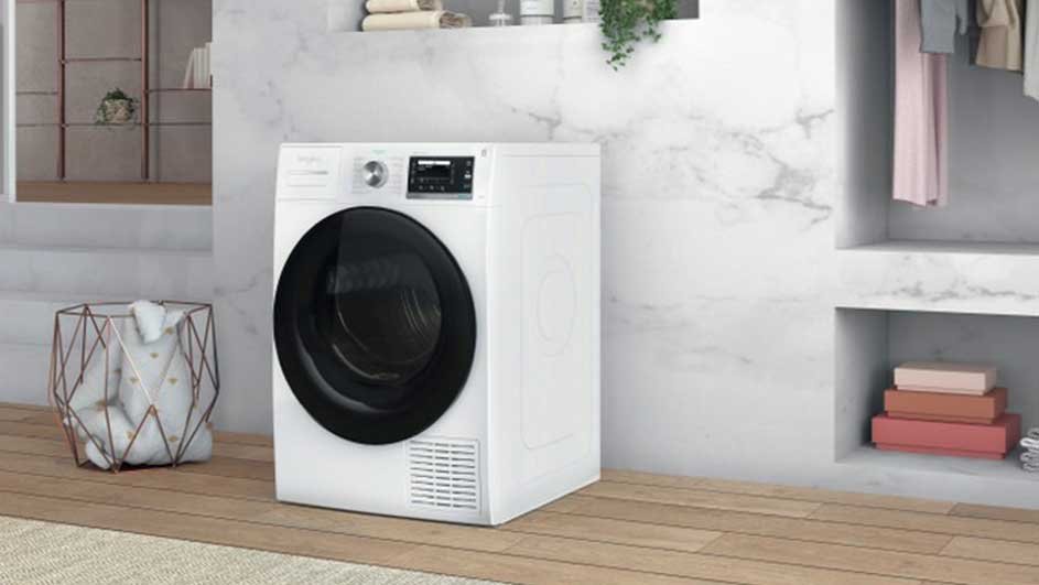 Een witte droogkast staat in een kamer met houten vloeren en een marmeren muur. Planken zijn gevuld met handdoeken en dozen.