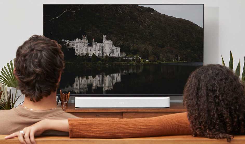 Twee mensen zitten ontspannen op een bank en kijken naar een groot scherm met een kasteel aan een donker meer.