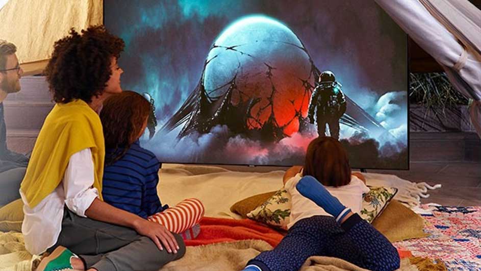 Een familie kijkt naar een tv in een tent. Op het scherm is een ruimtethema te zien met een beschadigd ruimteschip en een astronaut.
