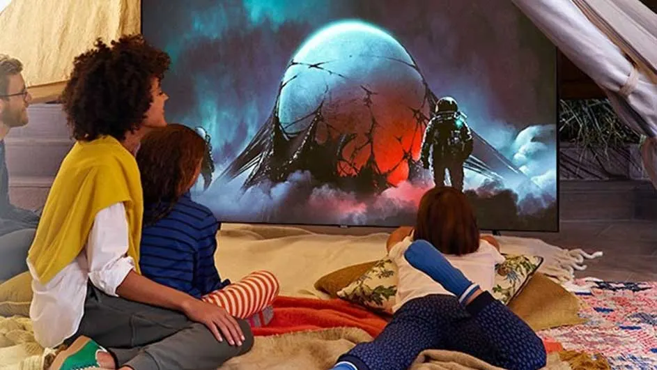 Een familie kijkt naar een tv in een tent. Op het scherm is een ruimtethema te zien met een beschadigd ruimteschip en een astronaut.