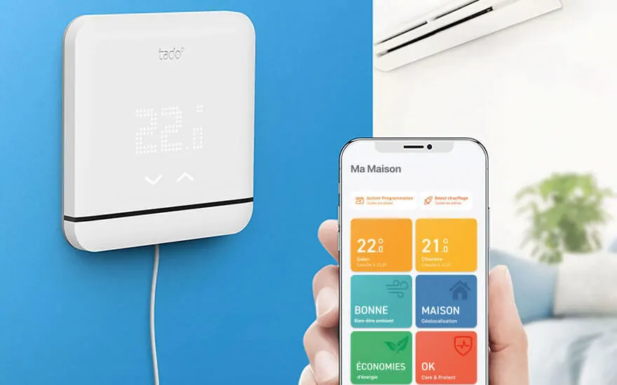 Een witte slimme thermostaat hangt aan een blauwe muur naast een smartphone. De app toont kamertemperaturen en gekleurde tegels voor huisfuncties.