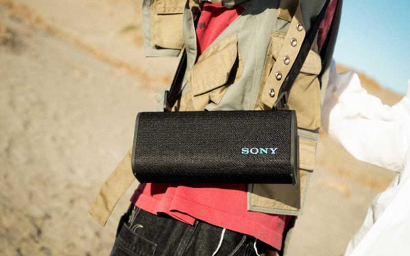 Une personne porte une enceinte portable Sony noire en bandoulière lors d’une activité en extérieur.