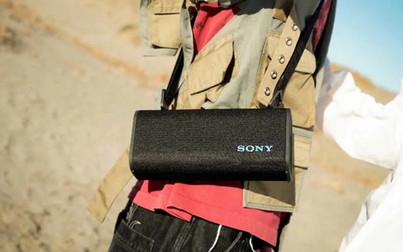 Une personne porte une enceinte portable Sony noire en bandoulière lors d’une activité en extérieur.