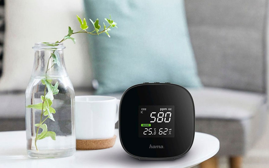 Een zwarte CO2-meter geeft 580 ppm aan, naast een vaas met plant en een witte beker op een tafel.