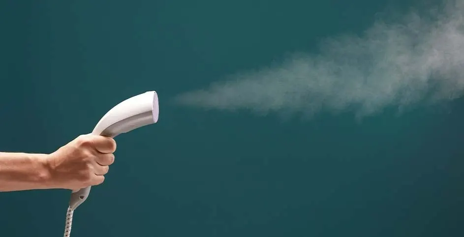 Un homme tient un défroisseur blanc qui dégage de la vapeur sur un fond vert.