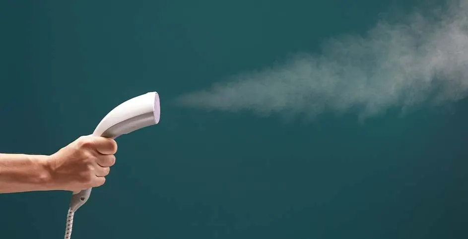 Een hand houdt een wit stoomstrijkijzer vast tegen een blauwgroene achtergrond, met stoom die naar rechts spuit.