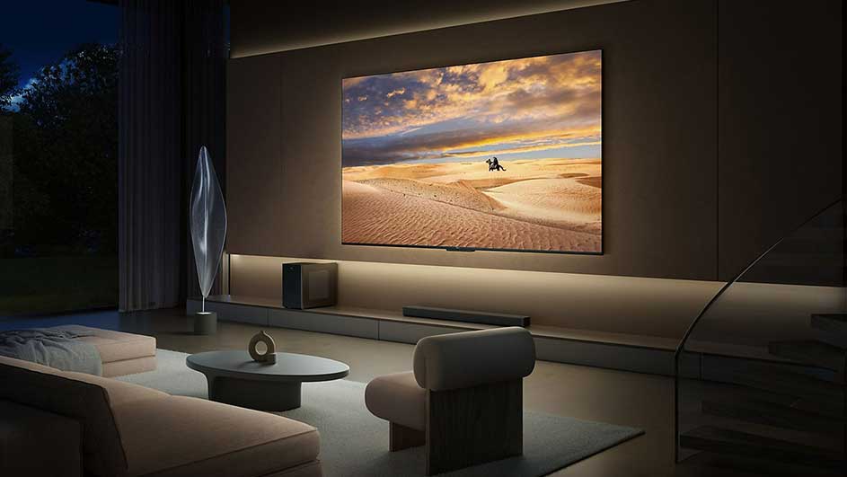 Woonkamer met tv waarop een zonsondergang te zien is boven een zandlandschap. Er staat een ronde tafel en een stoel.