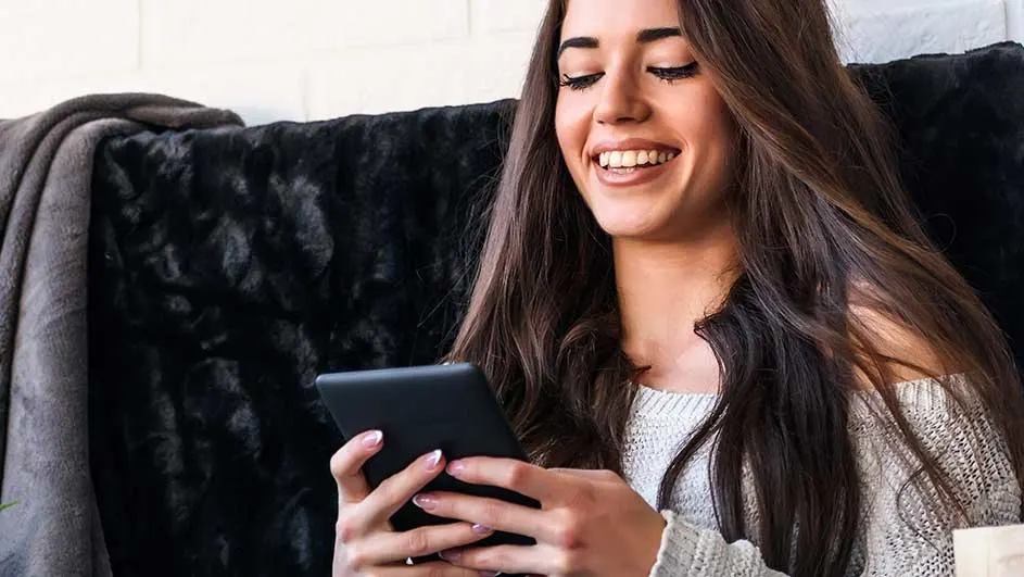 Een zwart tablet wordt vastgehouden tegen een achtergrond van een donkere sofa en een beige deken.