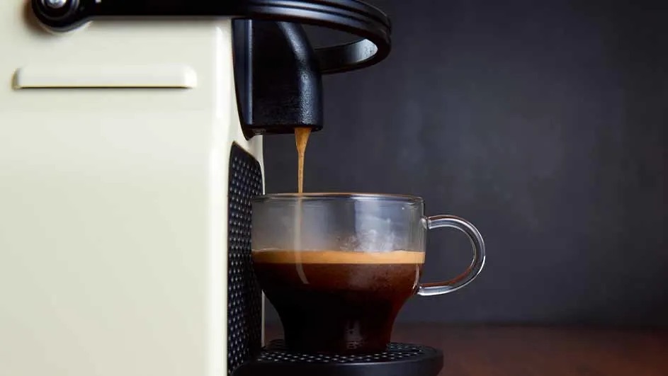 Espresso machine pouring coffee into a clear glass mug on a dark brown surface.