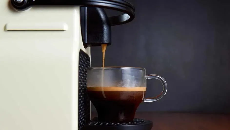 Espresso machine pouring coffee into a clear glass mug on a dark brown surface.