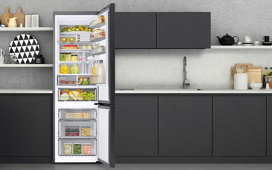 Un réfrigérateur ouvert, rempli de divers aliments, est placé dans une cuisine moderne aux armoires sombres et plans de travail clairs.