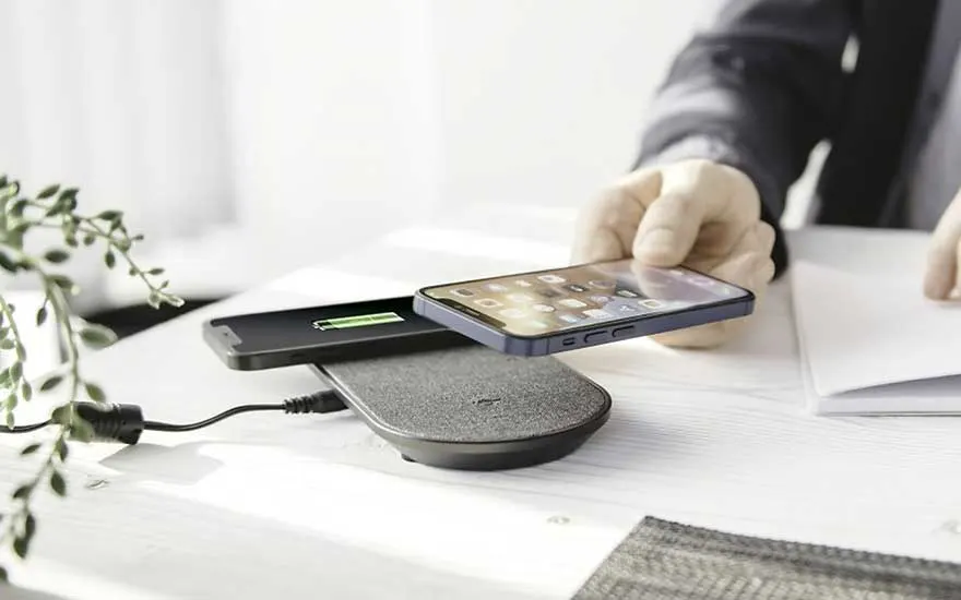 Deux téléphones sur un chargeur sans fil gris. Un téléphone charge ; l'autre est tenu à la main. Câble noir visible.