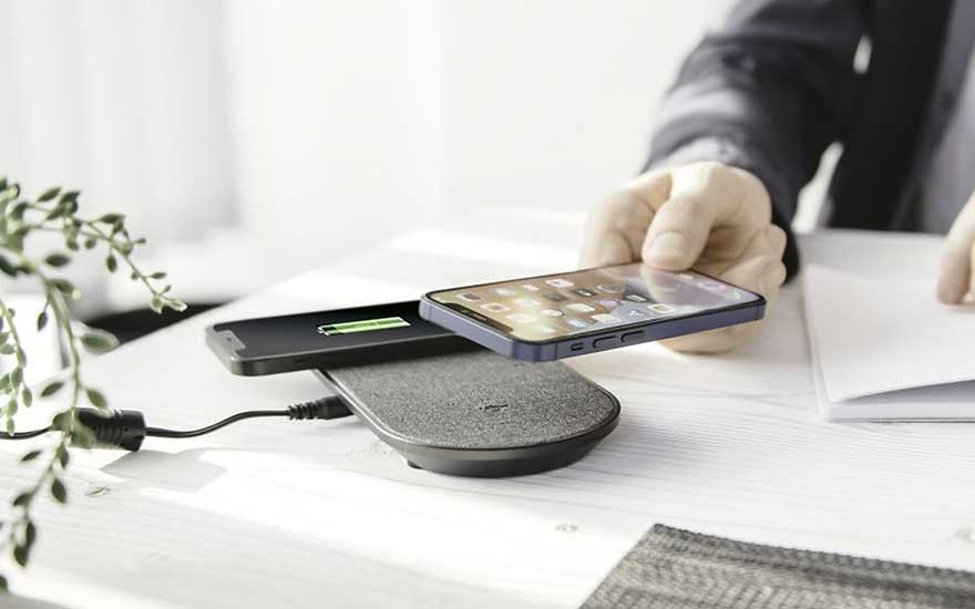 Een draadloze oplader met twee telefoons, waarvan één in de hand wordt gehouden, op een witte tafel.