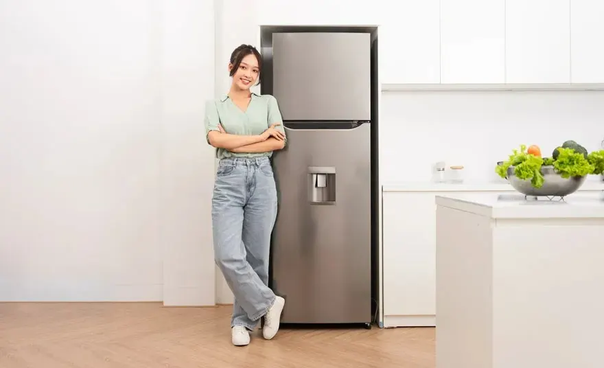 Dans une cuisine, un réfrigérateur gris se trouve à côté d'un comptoir blanc avec un bol de légumes.