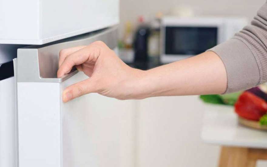 Een hand opent een witte kast in een keuken. Achteraan een microgolfoven en groenten.