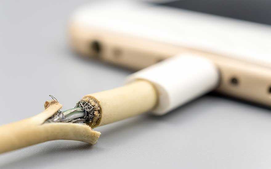Un câble de téléphone blanc usé est connecté à un téléphone sur une surface grise, montrant le câblage interne.