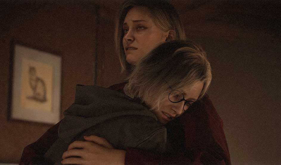 This is a video game. Two women hug in warm, dim light; the one with glasses clings tightly while the other looks away, worried and tense.