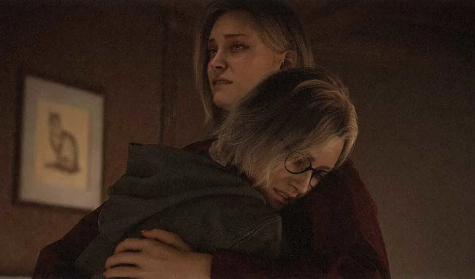 This is a video game. Two women hug in warm, dim light; the one with glasses clings tightly while the other looks away, worried and tense.