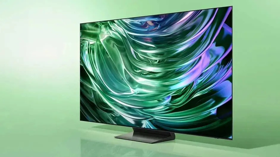 A modern Samsung TV stands on a green background, displaying an abstract image with green and purple glossy effects on the screen.