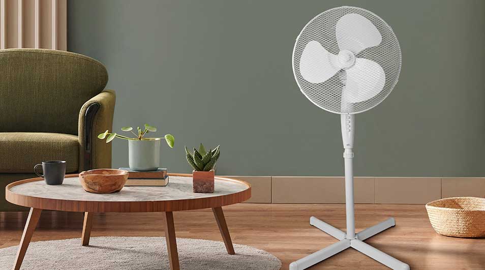 Een witte staande ventilator staat in een stijlvolle woonkamer naast een groene fauteuil, houten tafel en planten.