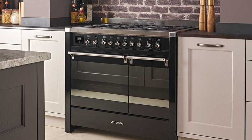 Een zwarte Smeg oven met draaiknoppen staat tussen witte keukenkasten in een keuken met een bakstenen muur.