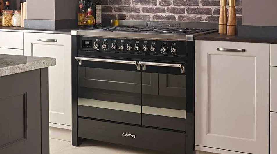 Een zwarte Smeg oven met draaiknoppen staat tussen witte keukenkasten in een keuken met een bakstenen muur.
