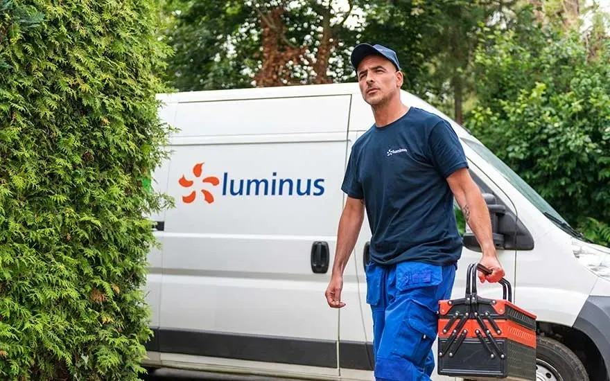 A white van with "Luminus" logo near a green bush. A toolbox is being held in front of the van.