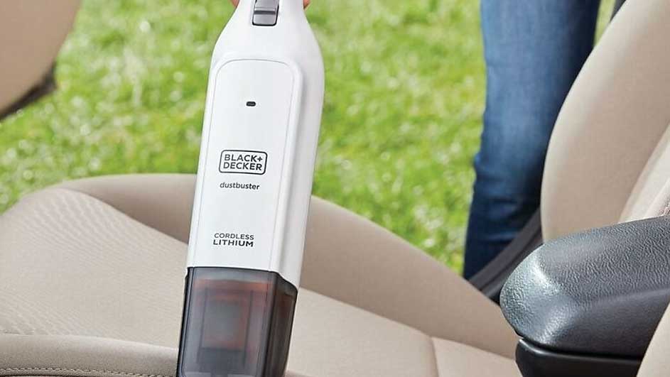 Een witte Black+Decker Dustbuster in een beige auto-interieur, met groene achtergrond.