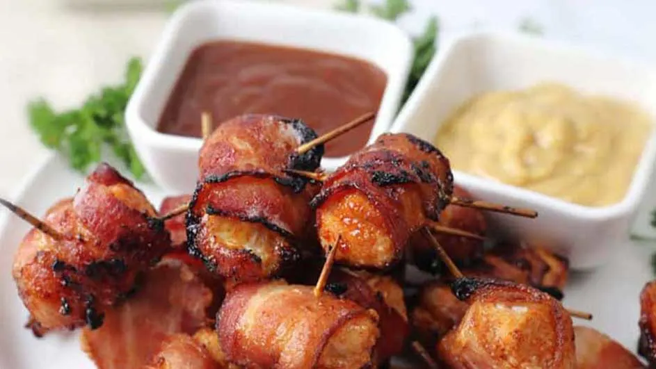 Brochettes de bacon caramélisé sur une assiette blanche, avec sauces brune et jaune en ramequins.