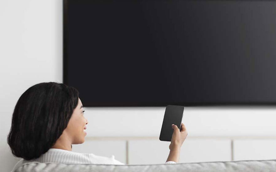 Een zwart televisiescherm hangt aan een witte muur. Iemand houdt een zwarte afstandsbediening vast.