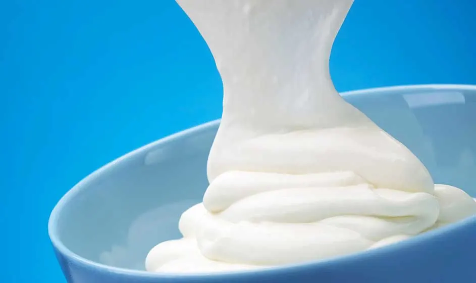 Une substance blanche, épaisse et crémeuse est versée dans un bol bleu pâle. Ses plis souples et sa texture lisse ressortent sur le fond bleu vif.
