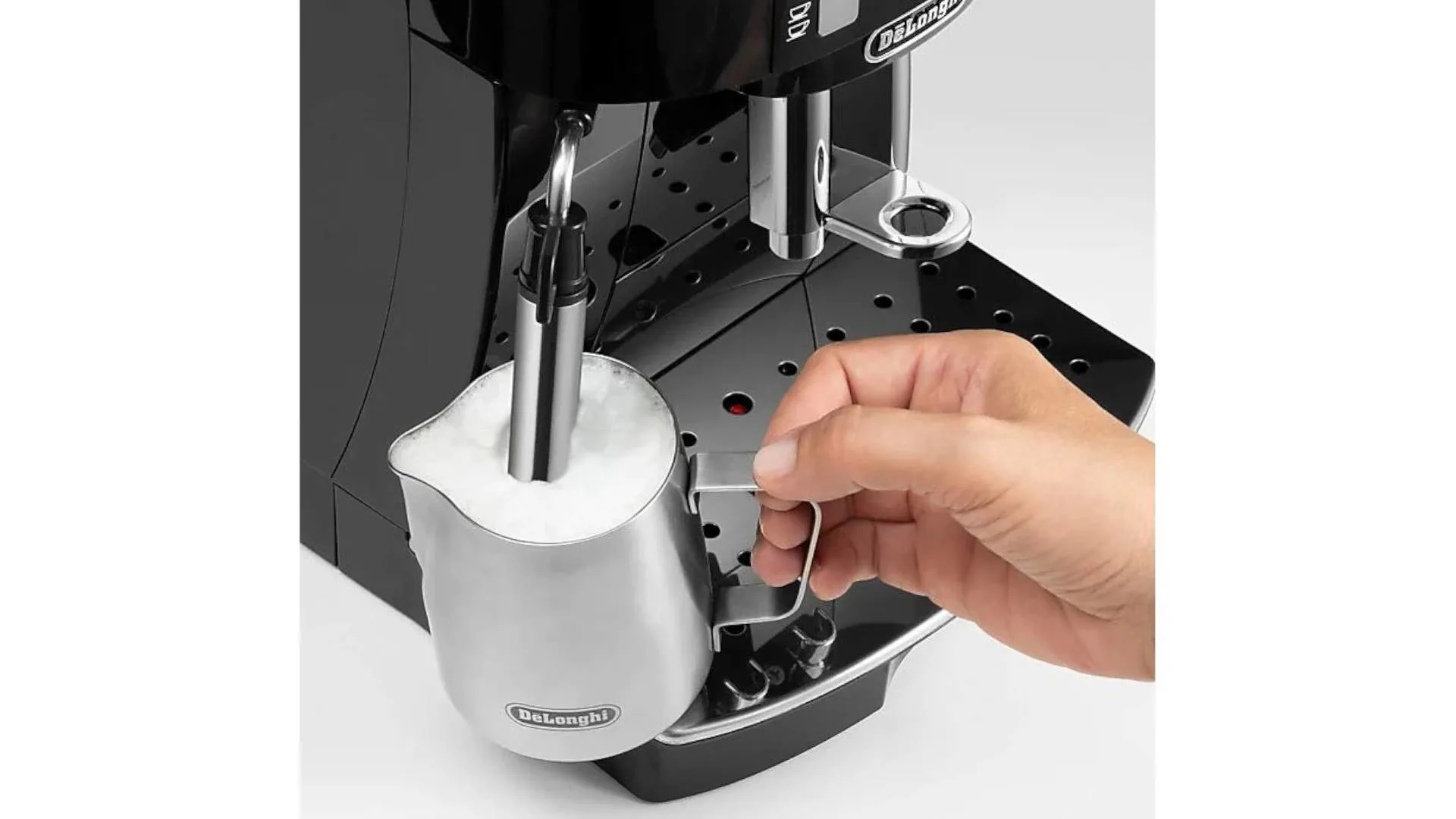 Une machine à expresso noire avec un pichet en métal rempli de lait moussant. Une main tient la poignée du pichet.
