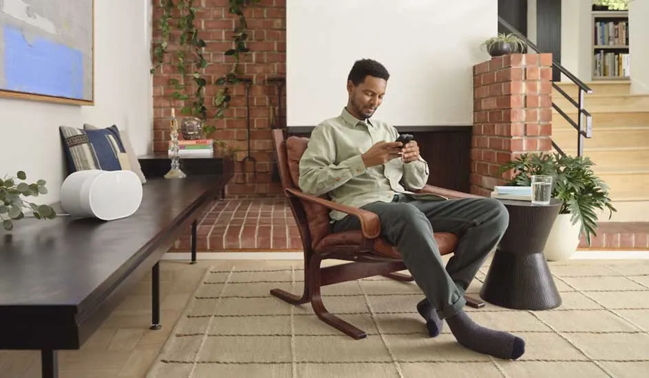 Salon lumineux avec fauteuil en cuir, table en bois, murs en briques et escalier. Plante verte et tapis à motifs.