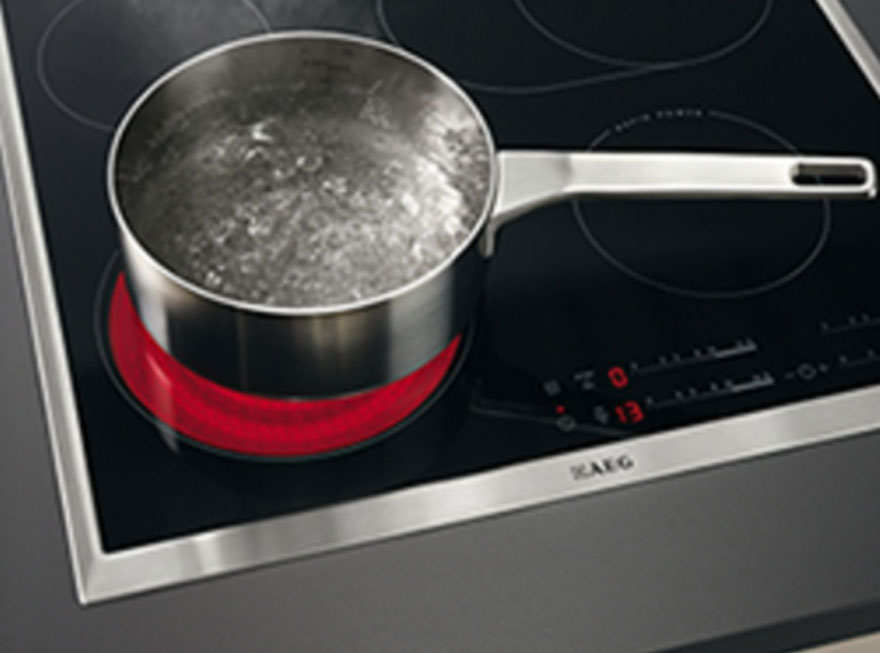 Casserole en métal avec de l'eau bouillante sur une plaque de cuisson noire avec un élément chauffant rouge.