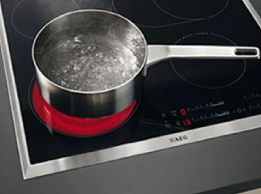 Casserole en métal avec de l'eau bouillante sur une plaque de cuisson noire avec un élément chauffant rouge.