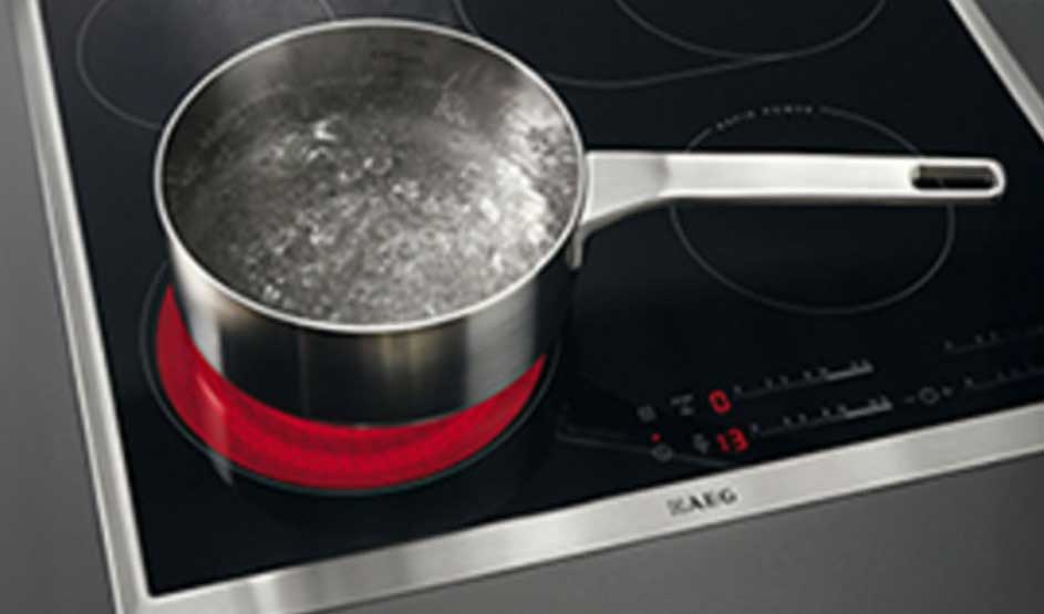 Casserole en métal avec de l'eau bouillante sur une plaque de cuisson noire avec un élément chauffant rouge.