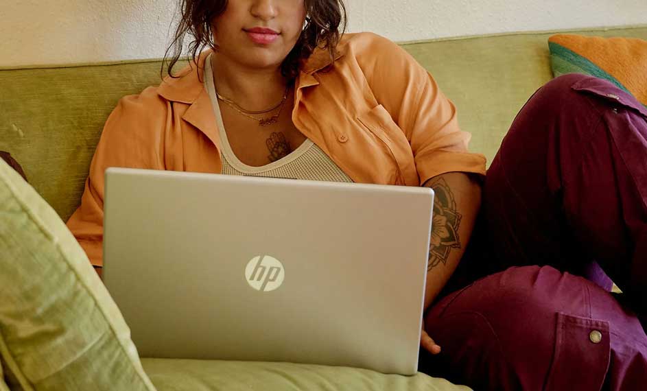 Laptop op een groene sofa met oranje kussen. De laptop is grijs en het HP-logo is zichtbaar.